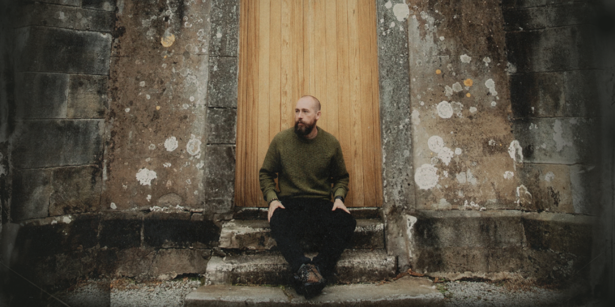 Darren Mulligan sitting at the doorway of an old irish stone building. Perhaps a church or a castle
