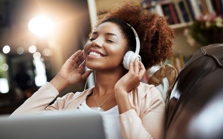 Shot of a young woman relaxing on the sofa and listening to music on her laptop